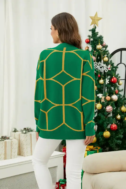 Emerald green knitted Christmas sweater with contrast color pattern worn by person near tree