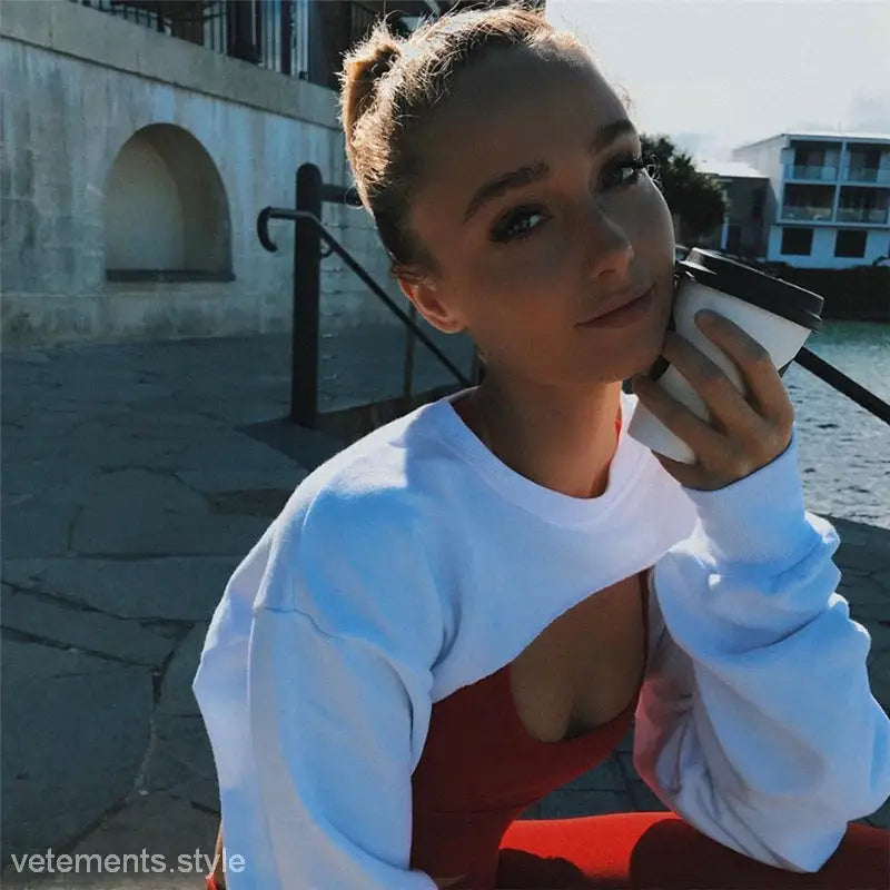 Young woman in a fashionable fringes sweater holding coffee near waterfront during spring or fall