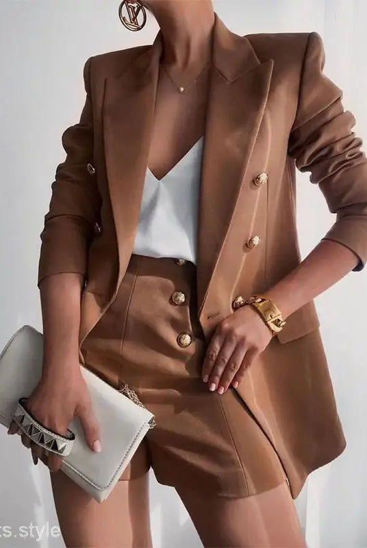 Brown tailored suit ensemble with white camisole and clutch, showcasing a high end jacket