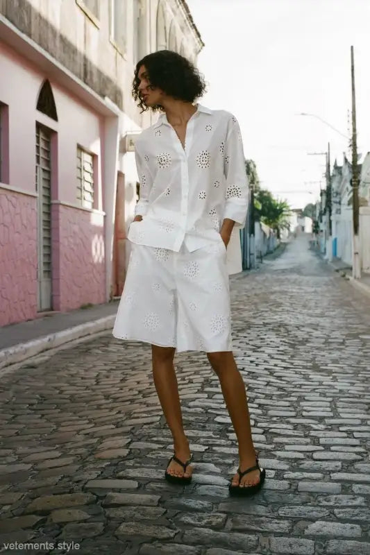 Woman in an all-white high waist casual hollow outfit with eyelet details on a cobblestone street