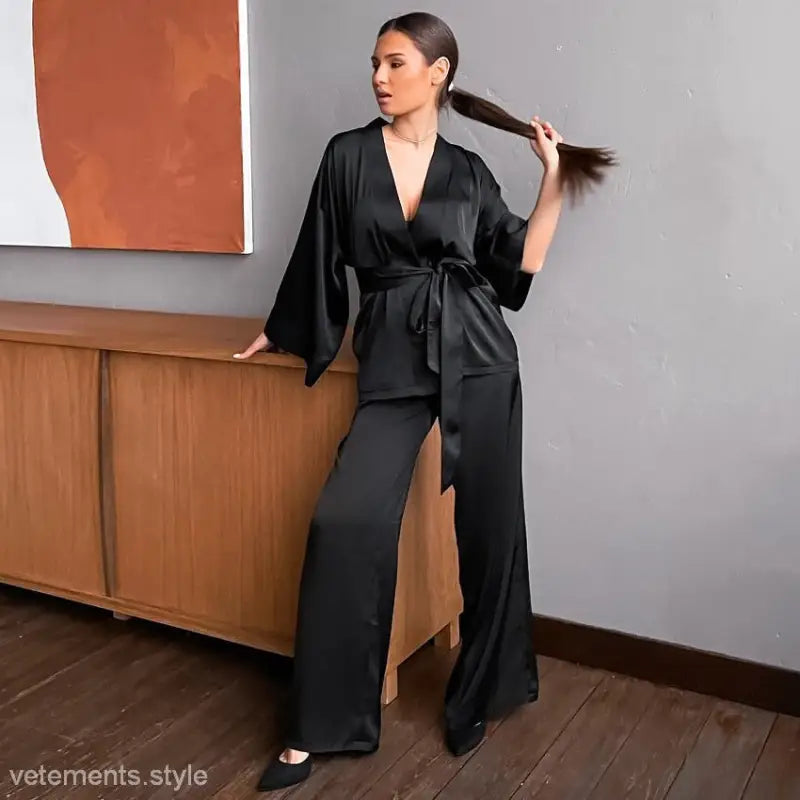 Woman wearing a black silk kimono-style jumpsuit with wide-leg pants, part of a casual satin pajamas set