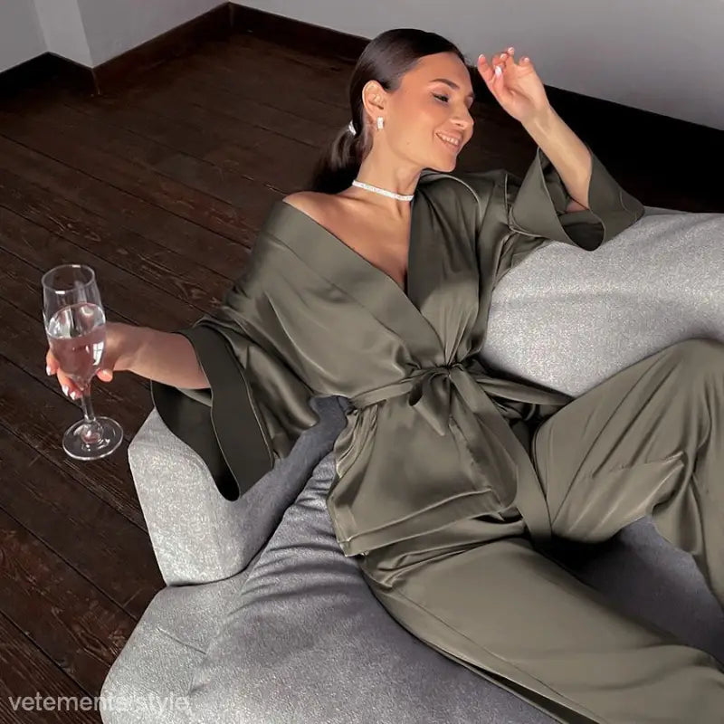 Woman in light brown casual satin pajamas set lounging with champagne on a couch