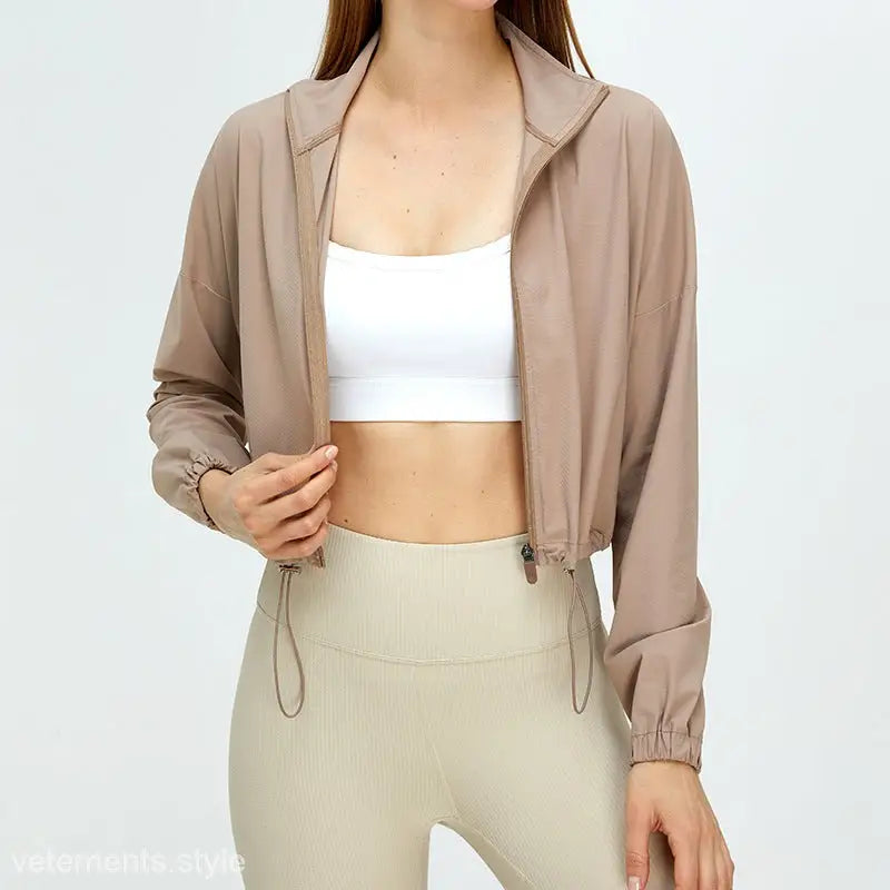 Cropped beige jacket over white crop top and light-colored leggings from running fitness clothes collection