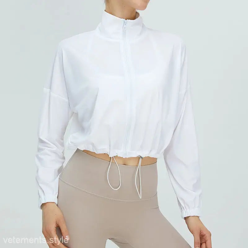 Cropped white zip-up jacket with drawstring hem over beige high-waisted leggings in running fitness clothes