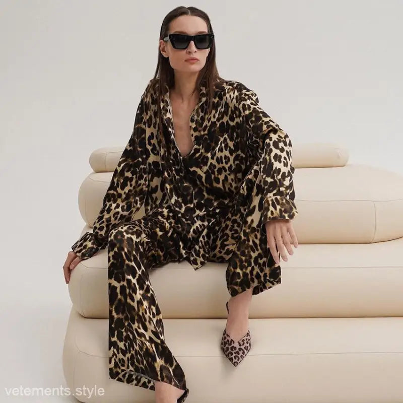 Woman in luxury leopard pajamas and sunglasses seated on cream couch showcasing light luxury leopard pajamas two-piece set