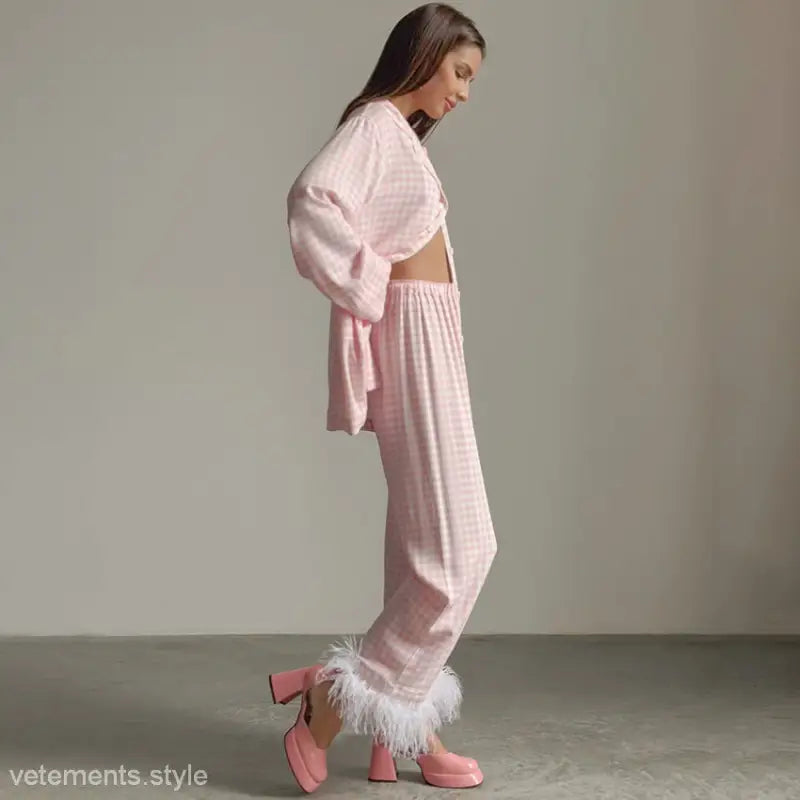 Woman wearing pink checkered loose satin loungewear with feather-trimmed pants and platform heels