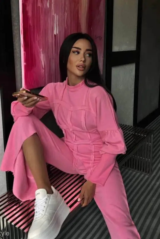 Woman in bright pink modern hoodie set with white sneakers on striped bench