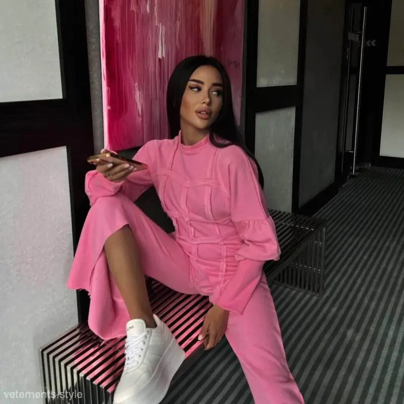 Woman in bright pink modern hoodie set with white sneakers on striped bench