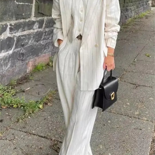 White suit ensemble with long blazer, wide-leg trousers, and black handbag for office style slim look