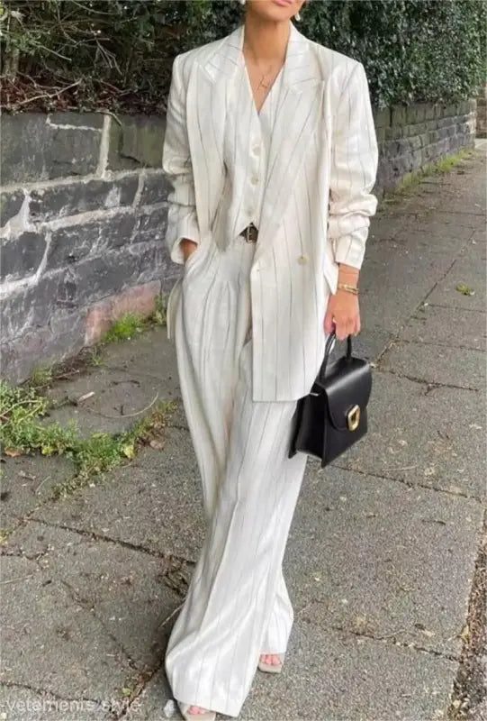 White suit ensemble with long blazer, wide-leg trousers, and black handbag for office style slim look