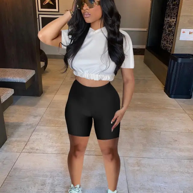 Woman in white crop top and black biker shorts, showcasing casual hoodie two piece set