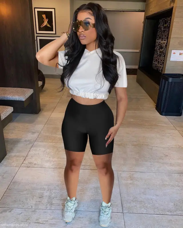 Woman in white crop top and black biker shorts, showcasing casual hoodie two piece set