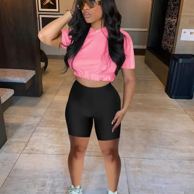 Woman in pink crop top and black bike shorts, showcasing casual hoodie two piece set
