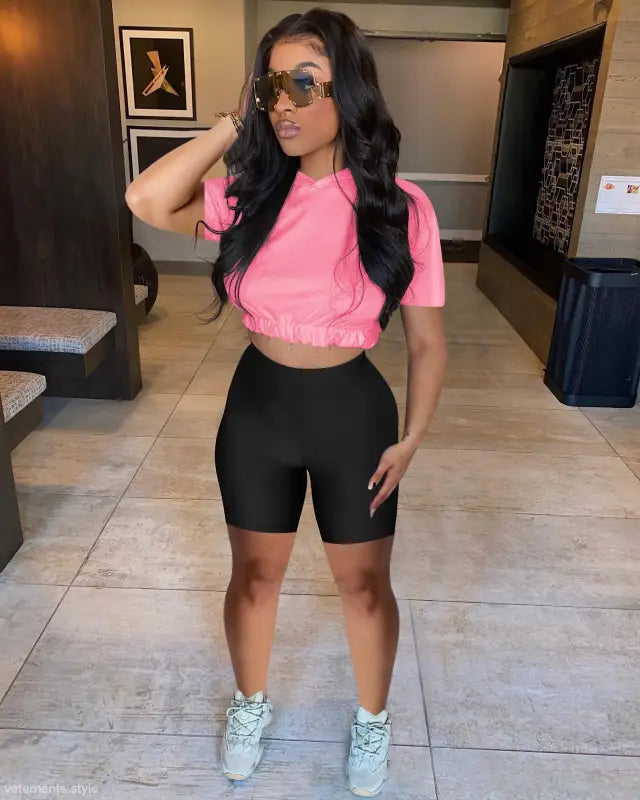 Woman in pink crop top and black bike shorts, showcasing casual hoodie two piece set
