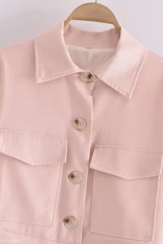 Pale pink button-up shirt with chest pockets hanging on wooden hanger for Pink Pants and Top Blazer High