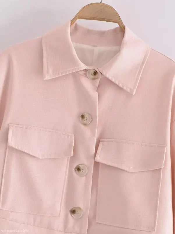 Pale pink button-up shirt with chest pockets hanging on wooden hanger for Pink Pants and Top Blazer High