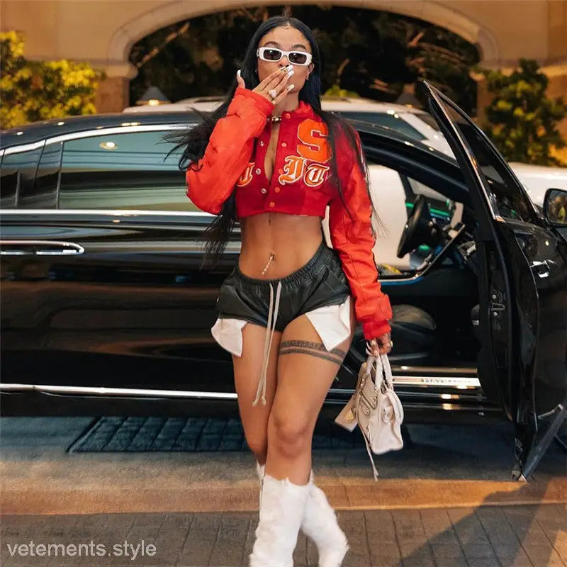Fashionable woman wearing a red crop top and black shorts with a round neck loose short varsity jacket featuring embroidery