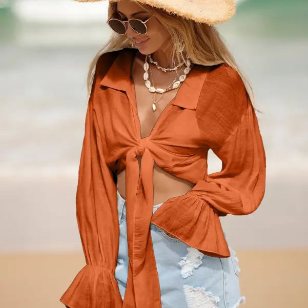 Woman in orange tie-front blouse and denim shorts with a straw hat for summer vacation