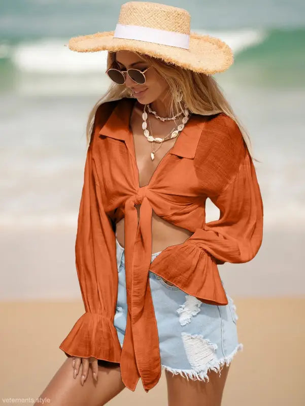 Woman in orange tie-front blouse and denim shorts with a straw hat for summer vacation