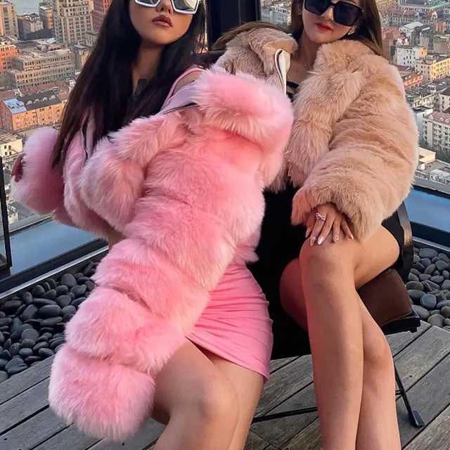 Two women in royal blue faux fur coats pose on balcony overlooking city