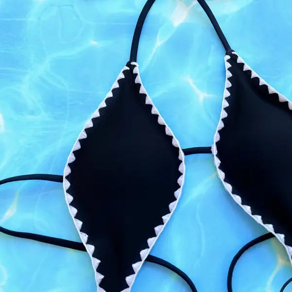 Black bikini top with white zigzag trim against a blue watery background.