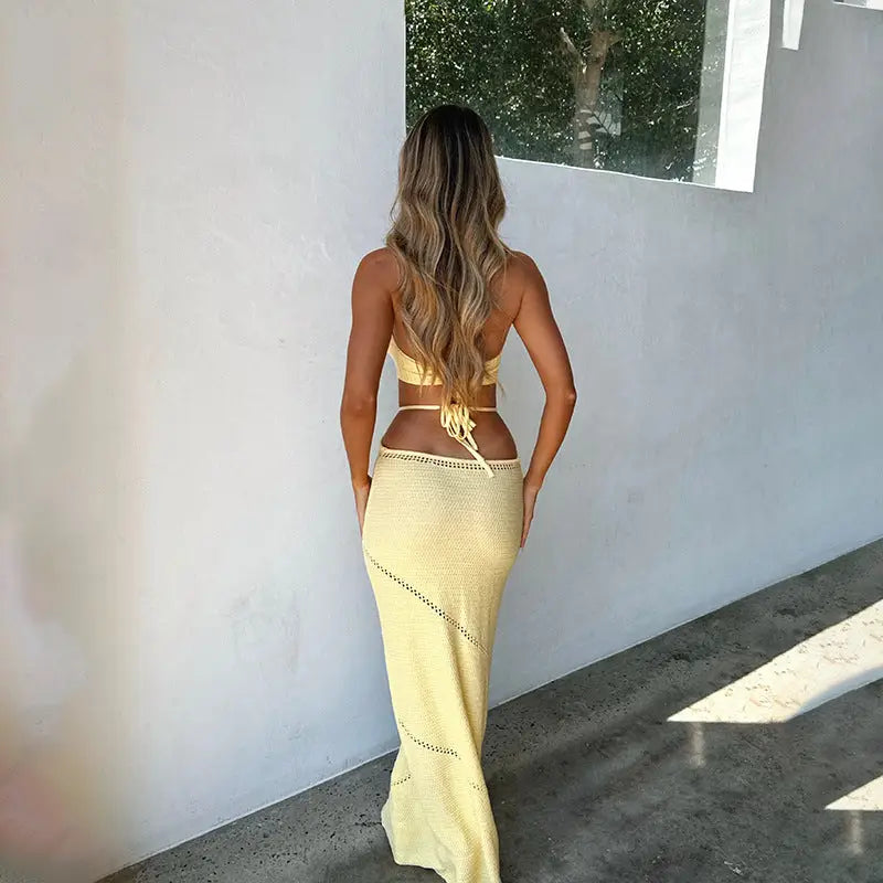 Woman in yellow knitted beach dress with cutout design and long skirt, view from behind