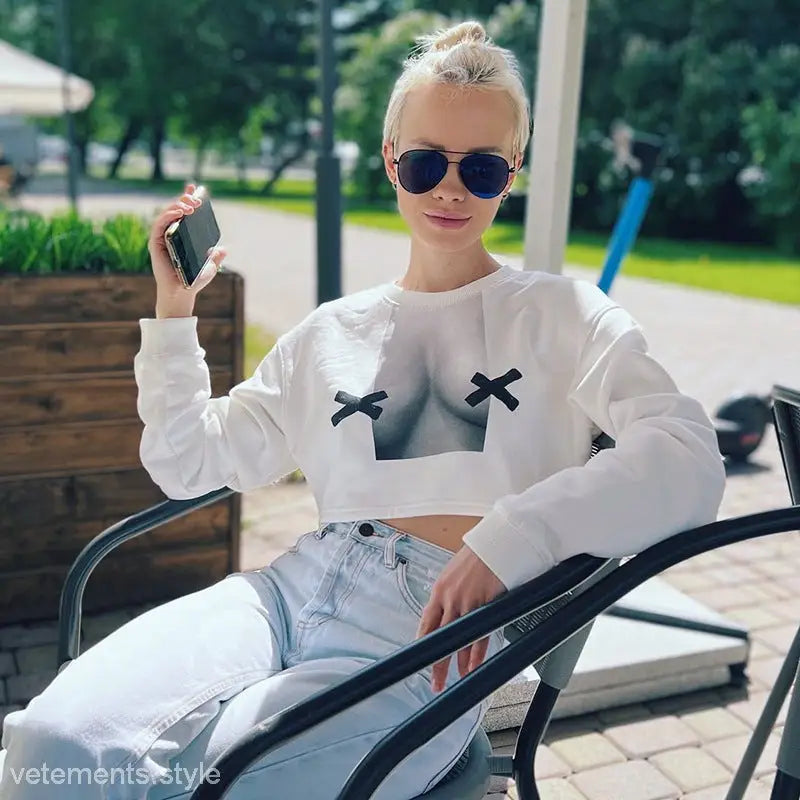 Person with blonde hair wearing a white cropped long sleeve pullover with graphic design