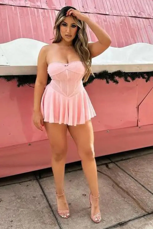 Woman wearing a short pink strapless dress posing against a pink background.