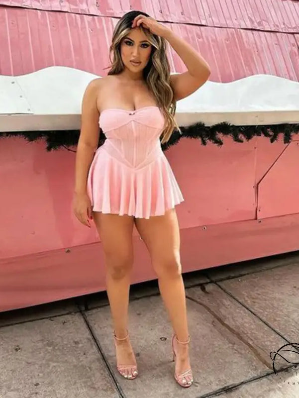 Woman wearing a short pink strapless dress posing against a pink background.