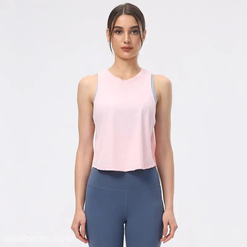 Woman wearing a light pink sleeveless top with blue leggings, showcasing the Sporty Nylon Half Waist Blouse in Chinese Olive Green and Midnight Blue
