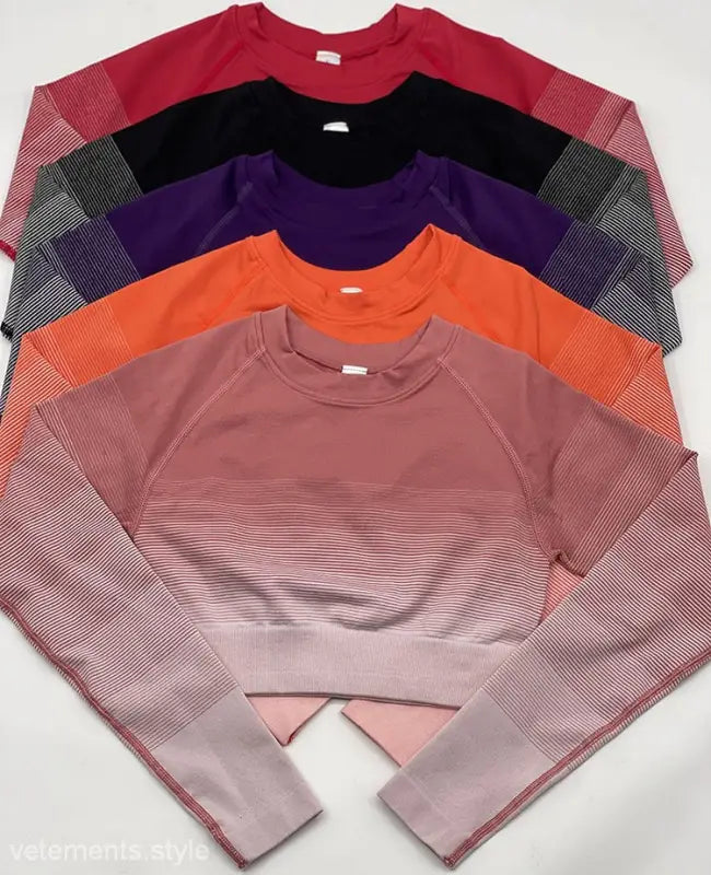 Stack of five athletic long-sleeved shirts with gradient and striped patterns, including purple long sleeve and orange pink pants