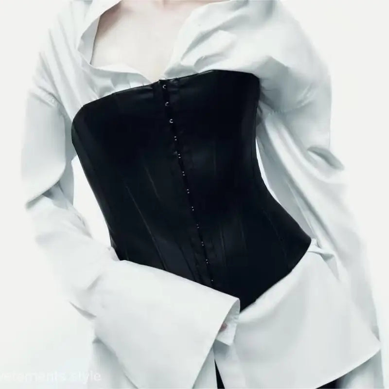 Black faux leather corset with hook-and-eye closures worn over a white shirt