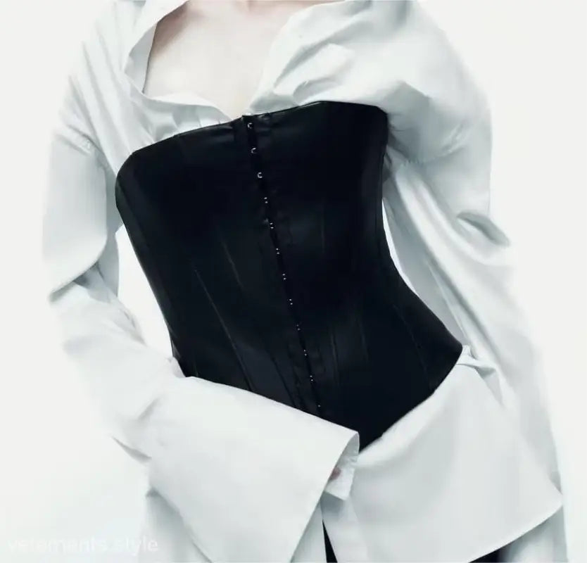 Black faux leather corset with hook-and-eye closures worn over a white shirt