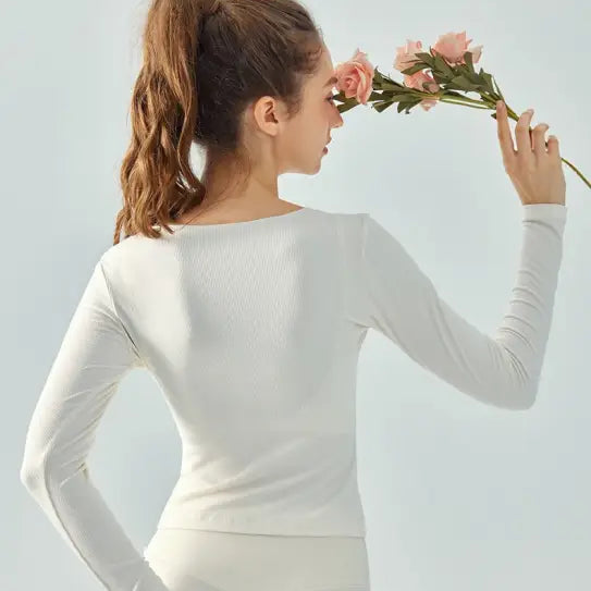 Woman in white athletic wear holding pink flowers wearing Wild Rose Yoga Tee in milk tea white