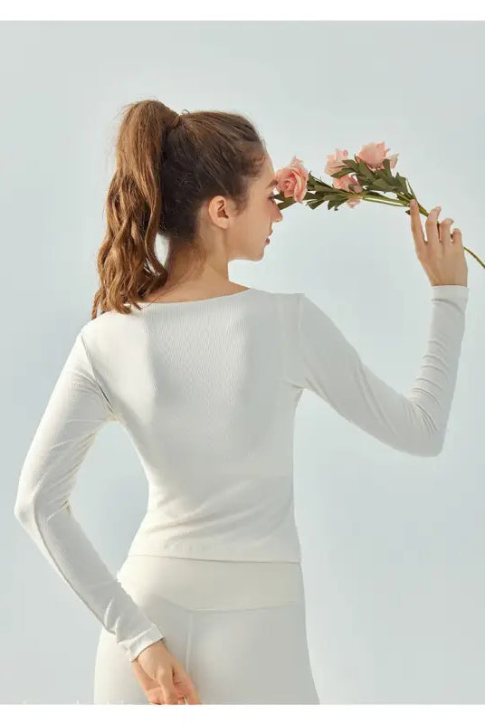 Woman in white athletic wear holding pink flowers wearing Wild Rose Yoga Tee in milk tea white