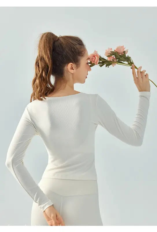 Woman in white athletic wear holding pink flowers wearing Wild Rose Yoga Tee in milk tea white