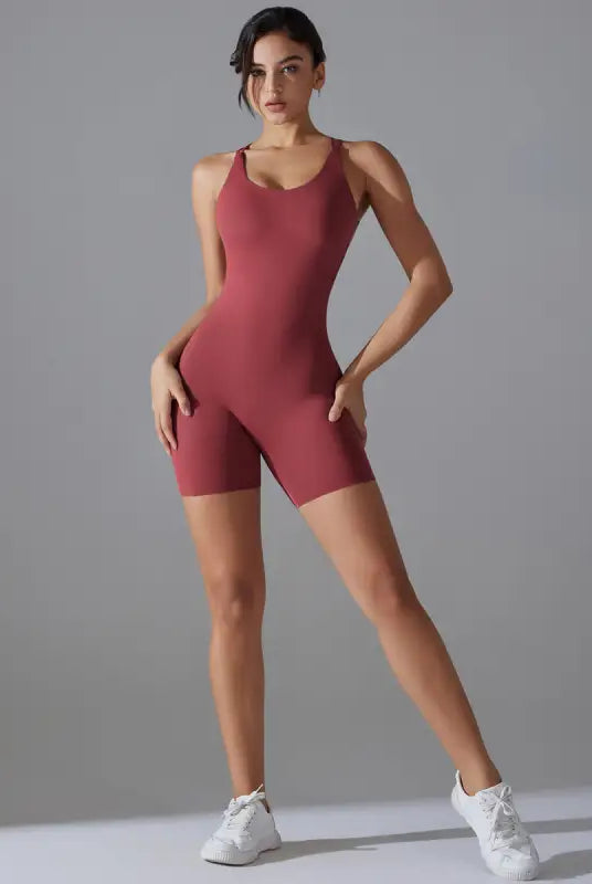 Woman wearing a burgundy sleeveless bodysuit and white sneakers.