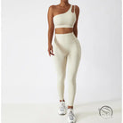 Cream-colored one-shoulder sports bra and high-waisted yoga pants set with white sneakers