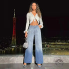 Woman in white fluffy crop top and high-waist denim trousers holding silver handbag