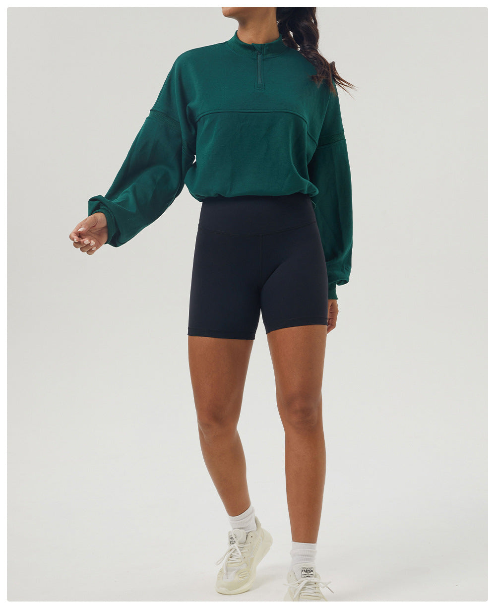 Woman in green long sleeve sweatshirt and black shorts, showcasing casual fitness fashion