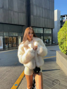 Short loose casual faux fur coat by Langry with cream color, black trim, and pockets