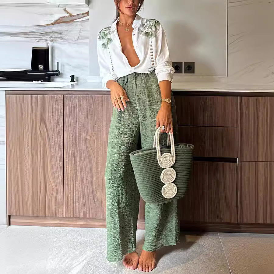 Woman in white shirt and green wide-leg trousers holding a green tote bag showcasing casual fashion and ملابس
