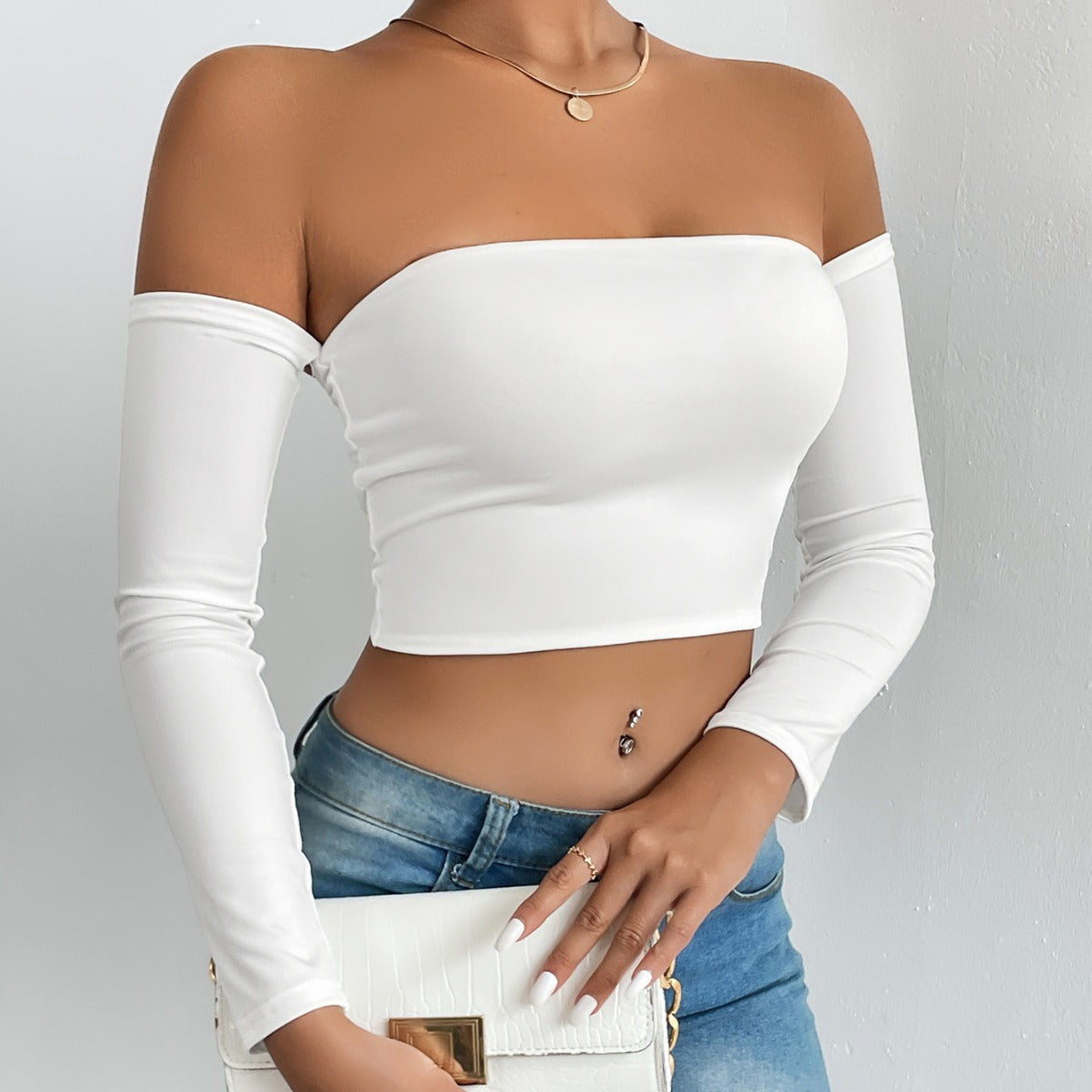 Fashionable woman wearing white off-shoulder crop top with blue jeans and white handbag