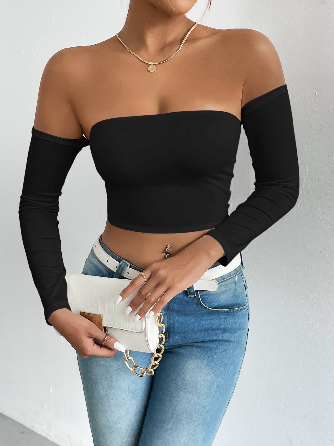 Fashionable woman in black off-shoulder camisole with blue jeans and white handbag