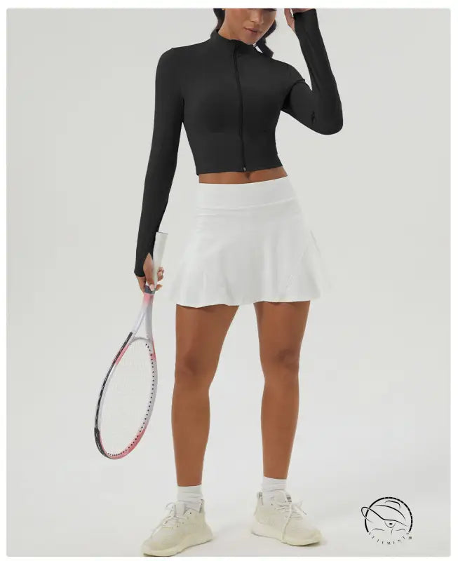 Woman in long sleeve sports jacket and white tennis skirt holding racket