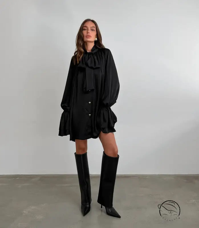 Elegant black satin dress with ruffles, long sleeves, and knee-high boots