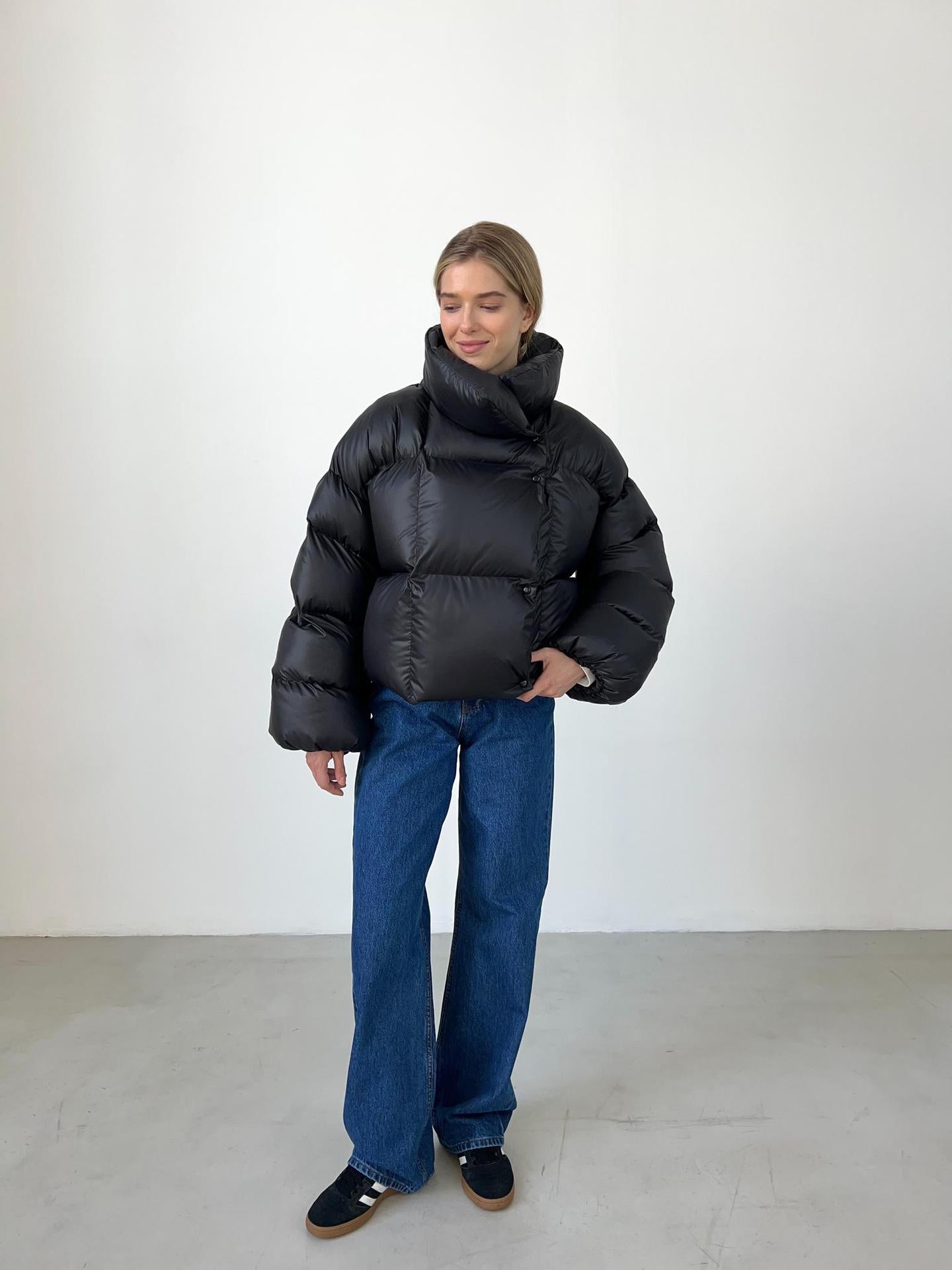 Woman in a black puffer jacket and blue jeans showcasing trendy fashion ملابس style
