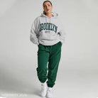 Woman in a white Brooklyn sweatshirt set with green sweatpants, featuring a casual style