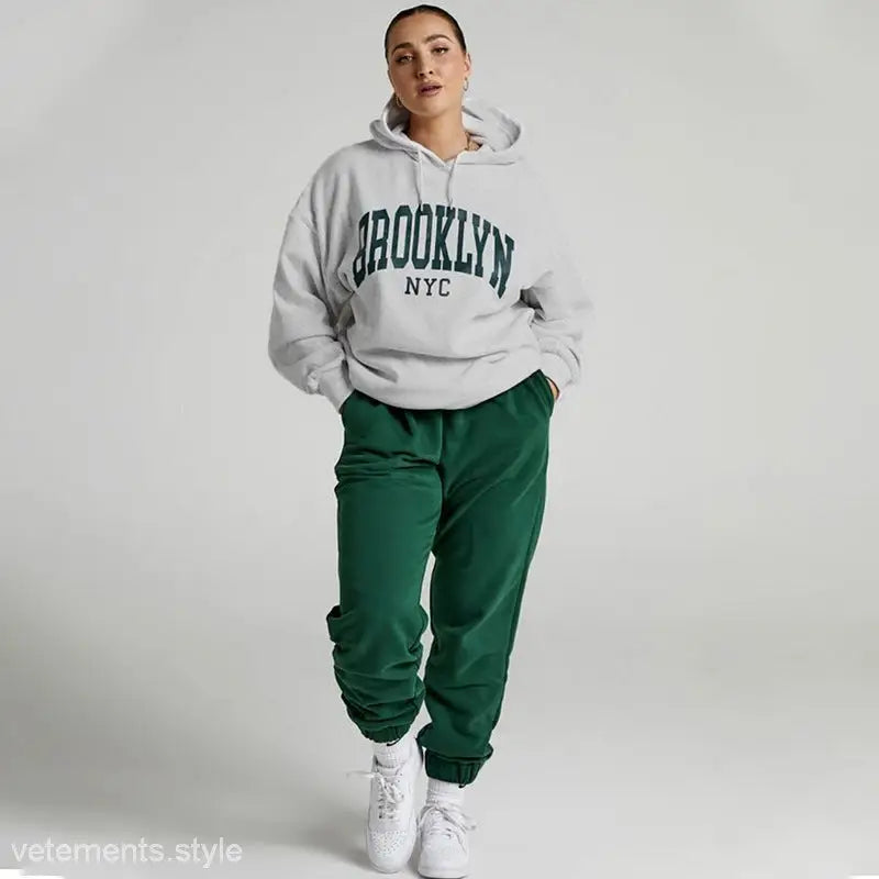Woman in a white Brooklyn sweatshirt set with green sweatpants, featuring a casual style
