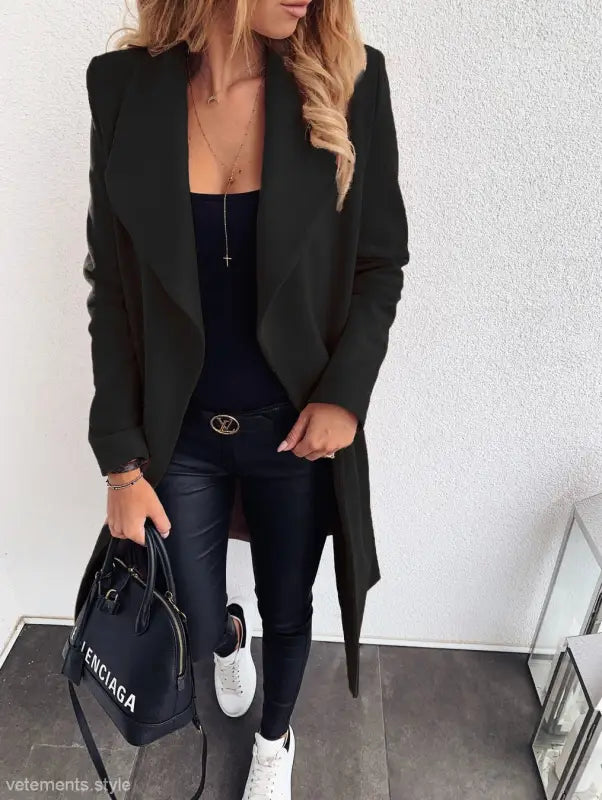 Black trench coat over dark outfit, paired with white sneakers and Balenciaga handbag